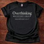 Black t-shirt with 'Overthinking Recovery Group Philippians 4:6-7' text on a wooden surface