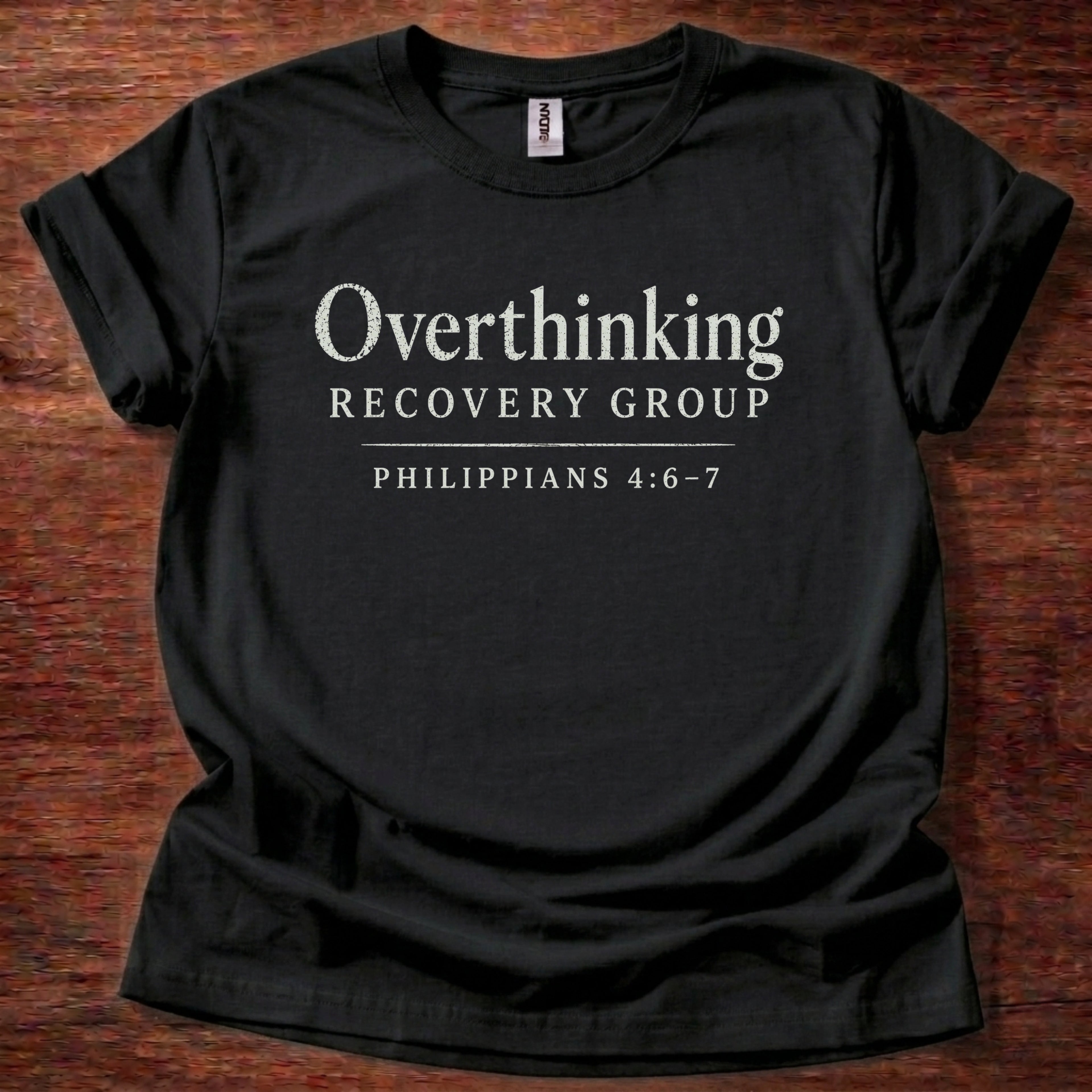 Black t-shirt with 'Overthinking Recovery Group Philippians 4:6-7' text on a wooden surface