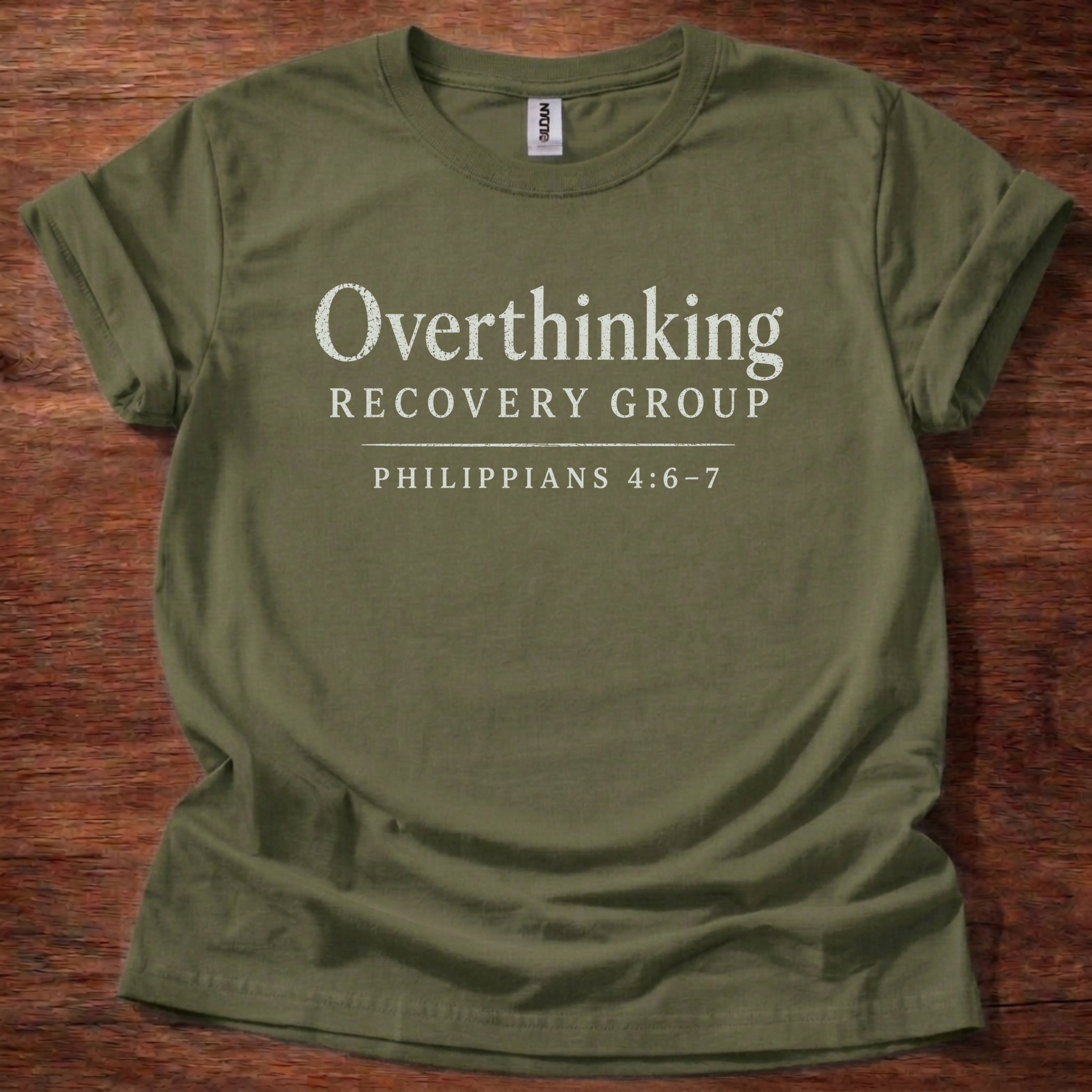Green t-shirt with 'Overthinking Recovery Group Philippians 4:6-7' text on a wooden surface
