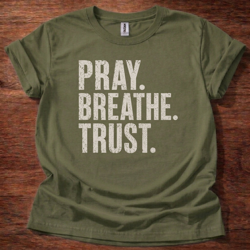 Green t-shirt with 'PRAY. BREATHE. TRUST.' text on a wooden surface