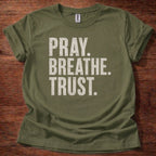 Green t-shirt with 'PRAY. BREATHE. TRUST.' text on a wooden surface