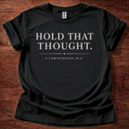 Black t-shirt with 'Hold That Thought' text on a wooden surface