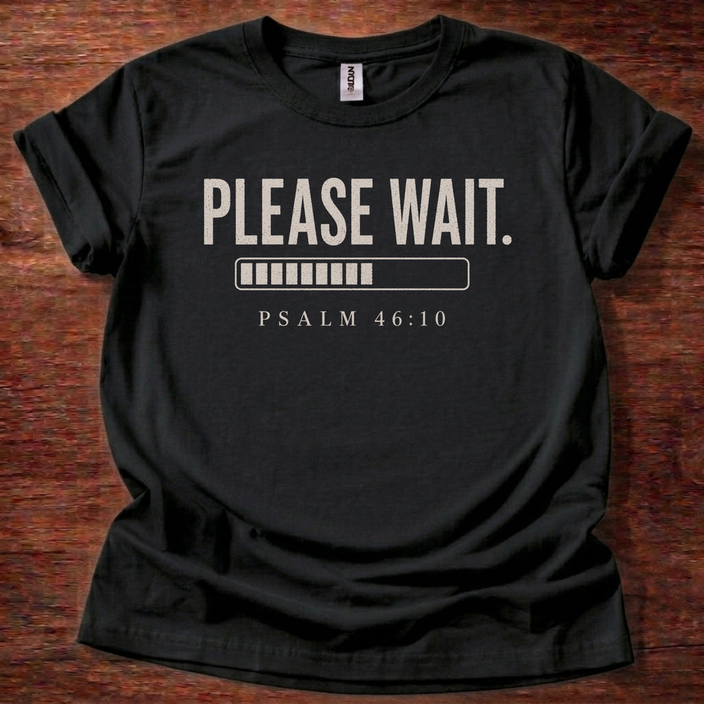 Black t-shirt with 'PLEASE WAIT. PSALM 46:10' text on a wooden surface