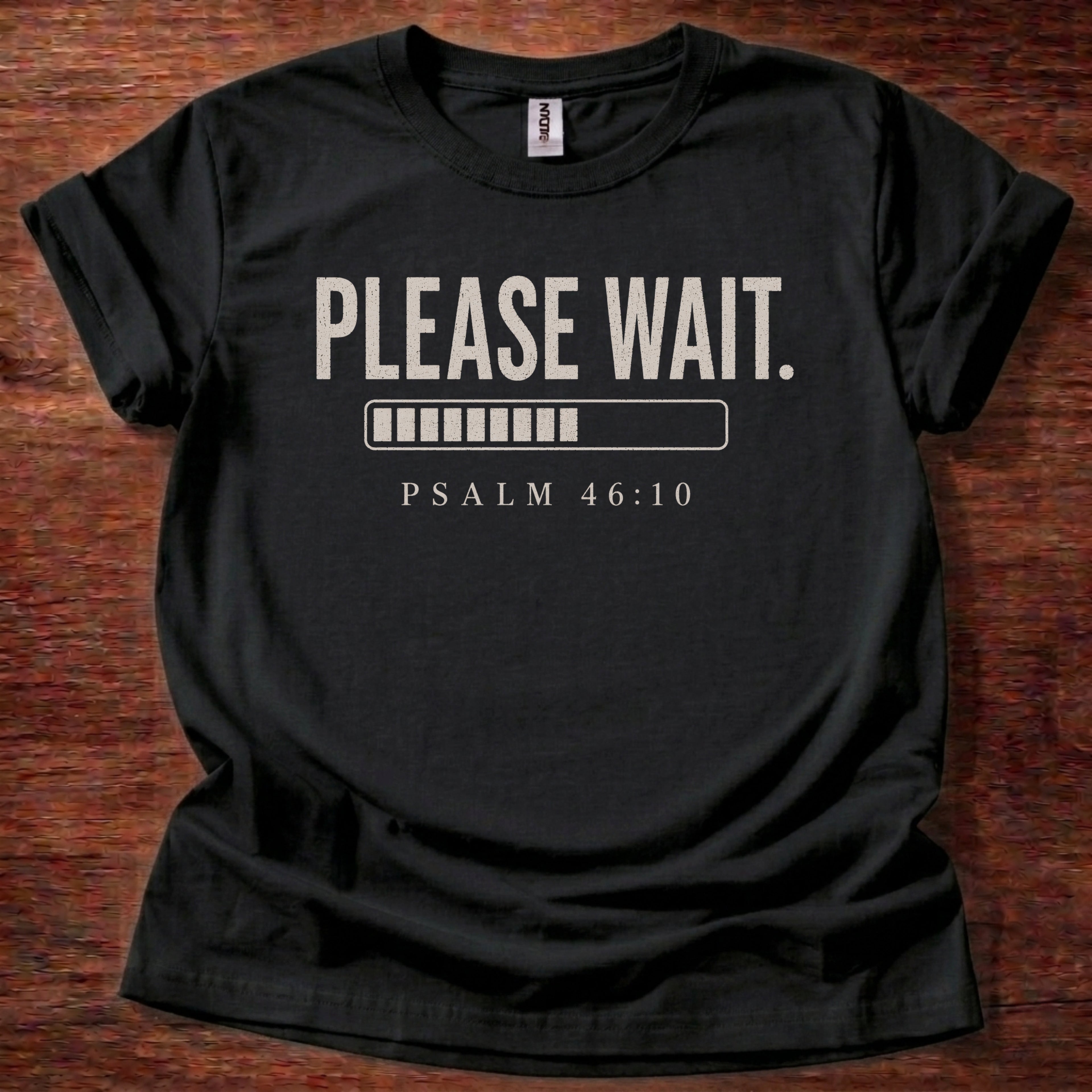 Black t-shirt with 'PLEASE WAIT. PSALM 46:10' text on a wooden surface