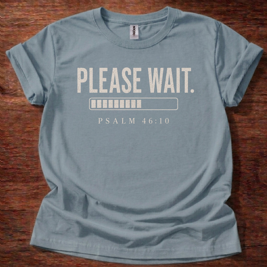 Blue t-shirt with 'Please Wait' and Psalm 46:10 text on a wooden surface