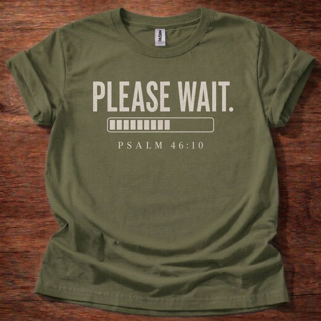 Green t-shirt with 'PLEASE WAIT. PSALM 46:10' text on a wooden surface