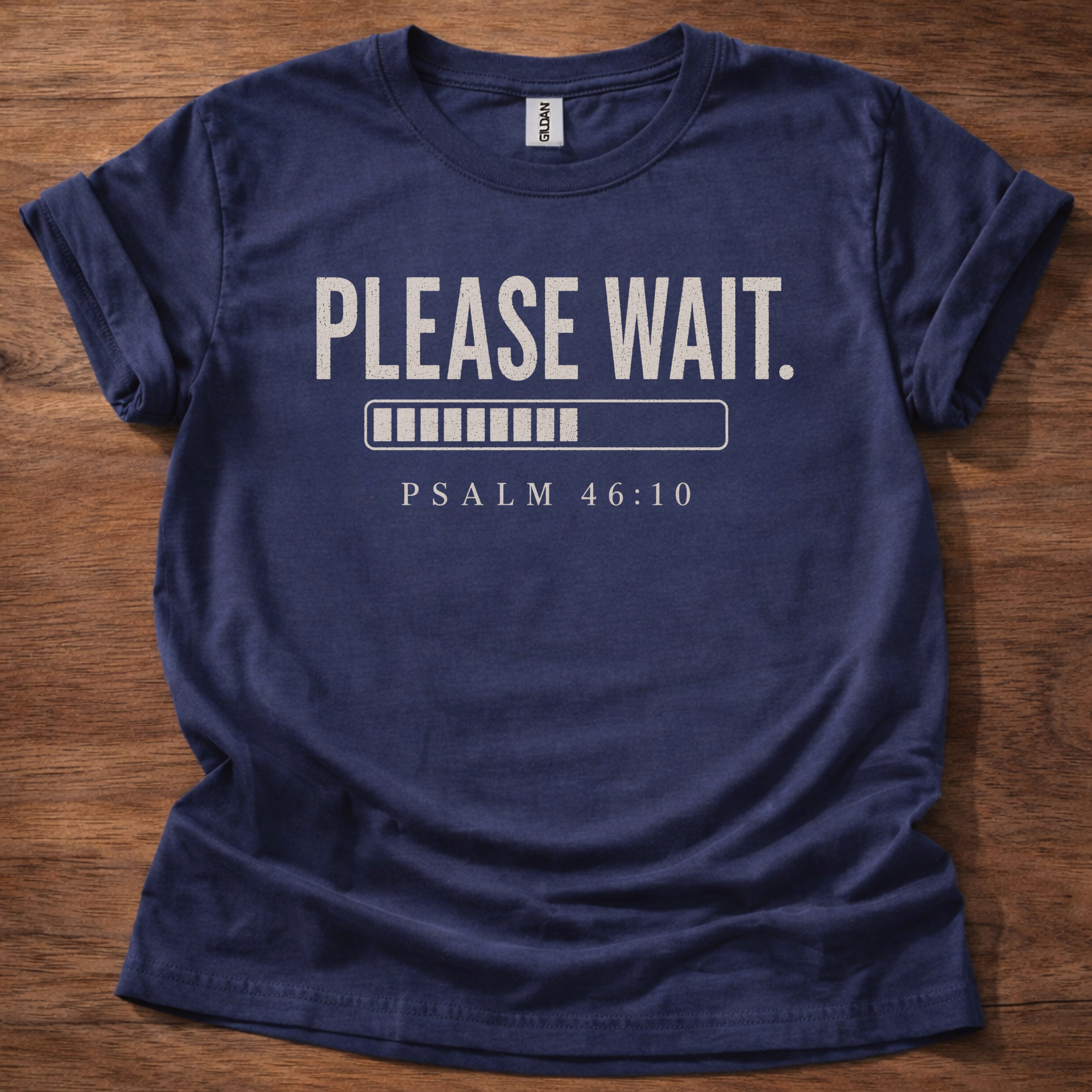 Navy blue t-shirt with 'PLEASE WAIT. PSALM 46:10' text on a wooden surface