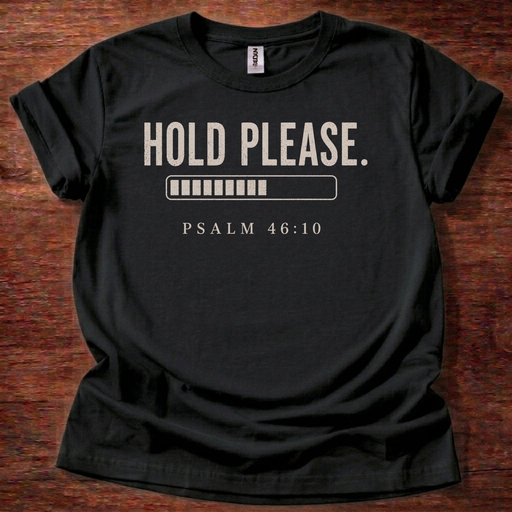 Black t-shirt with 'Hold Please. Psalm 46:10' text on a wooden surface