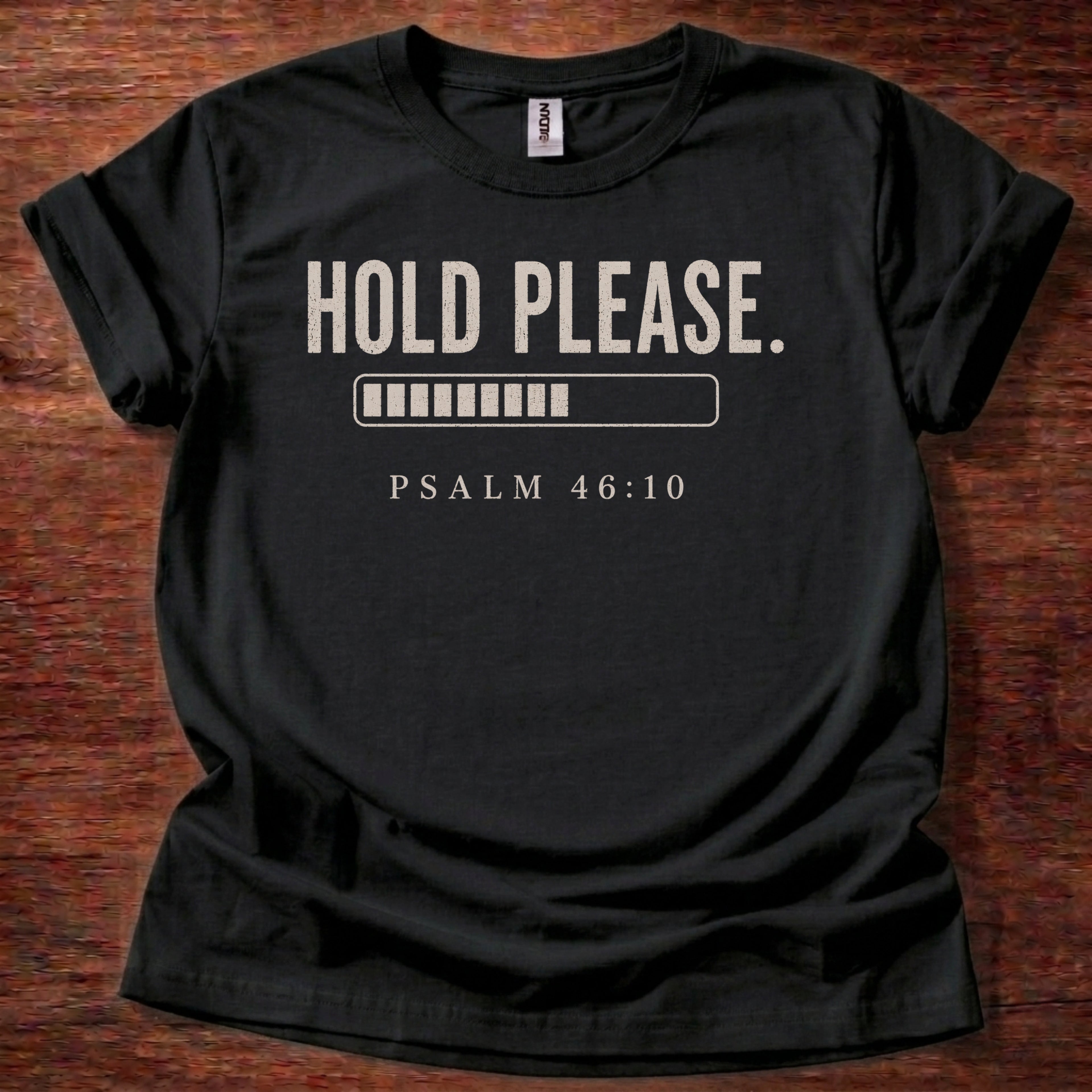 Black t-shirt with 'Hold Please. Psalm 46:10' text on a wooden surface