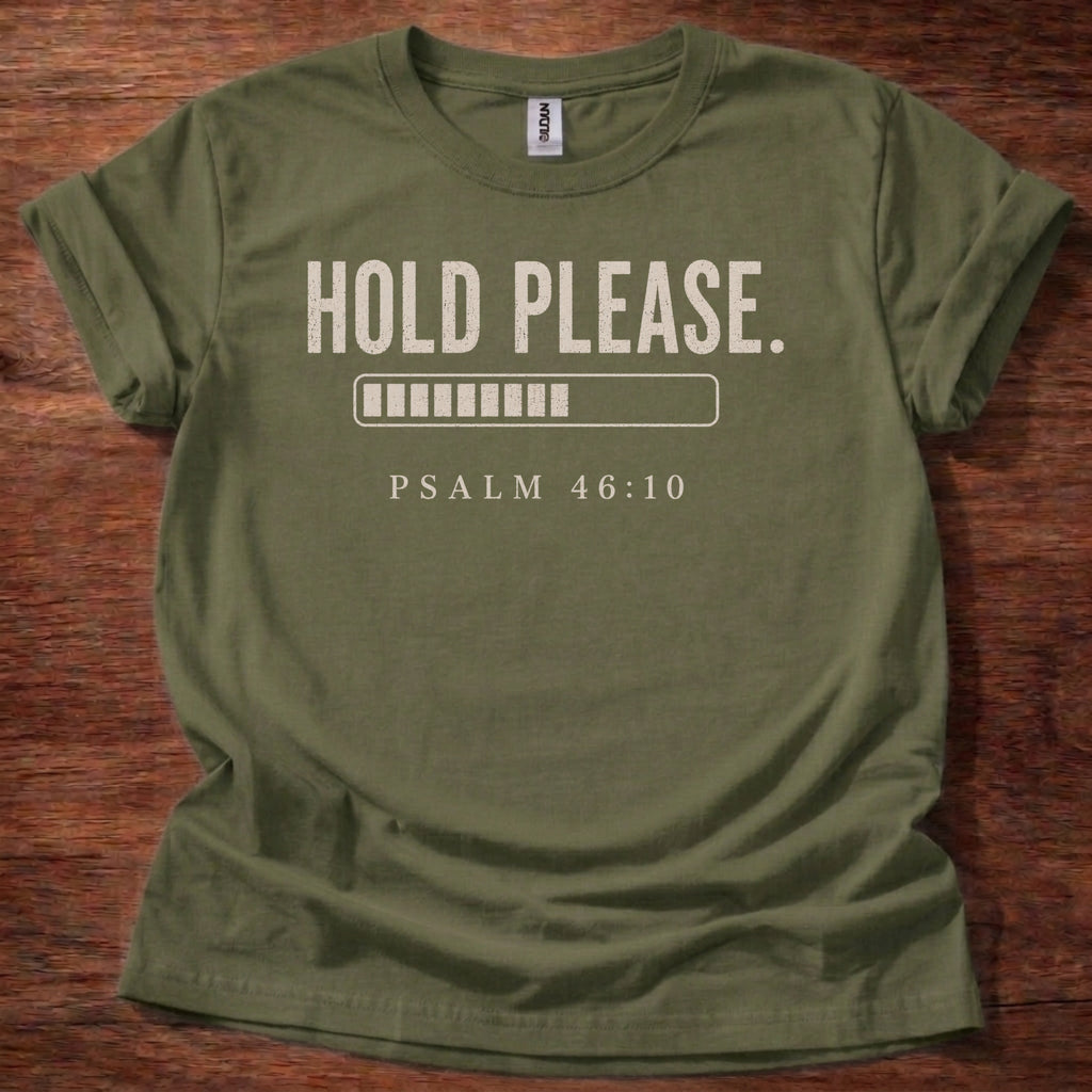 Green t-shirt with 'Hold Please. Psalm 46:10' text on a wooden surface