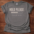 Gray t-shirt with 'Hold Please. Psalm 46:10' text on a wooden surface