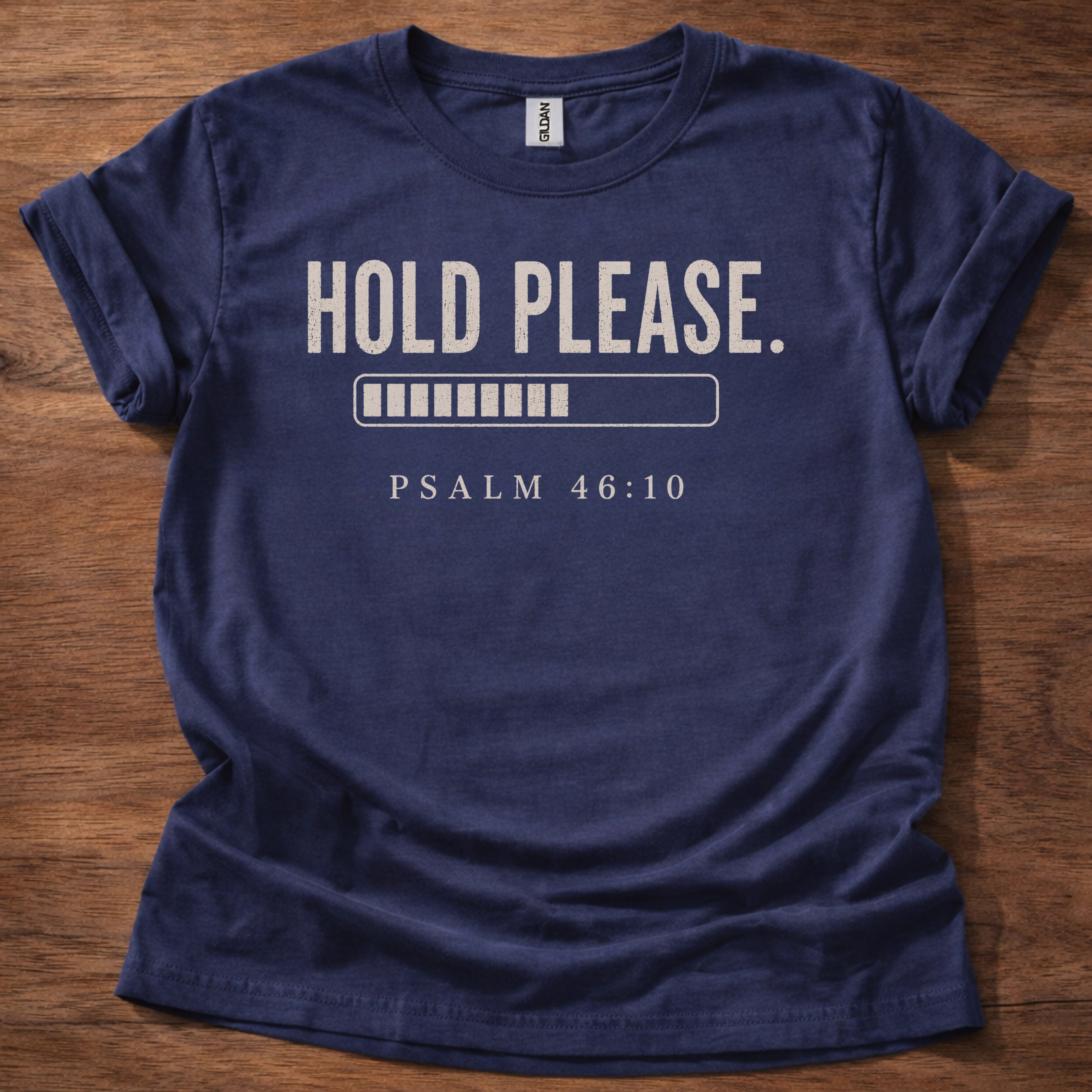 Navy blue t-shirt with 'Hold Please. Psalm 46:10' text on a wooden surface