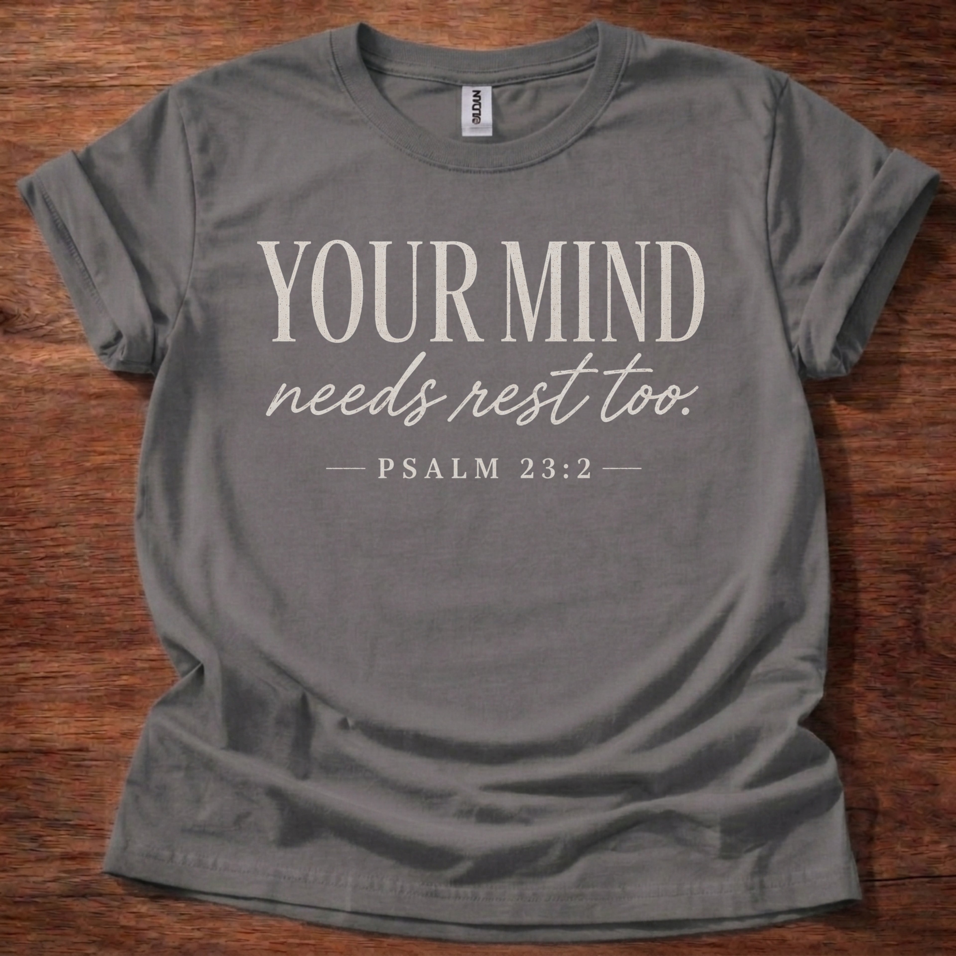 Gray t-shirt with 'Your Mind Needs Rest Too' text on a wooden surface