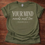 Green t-shirt with 'Your Mind Needs Rest Too' text on a wooden surface