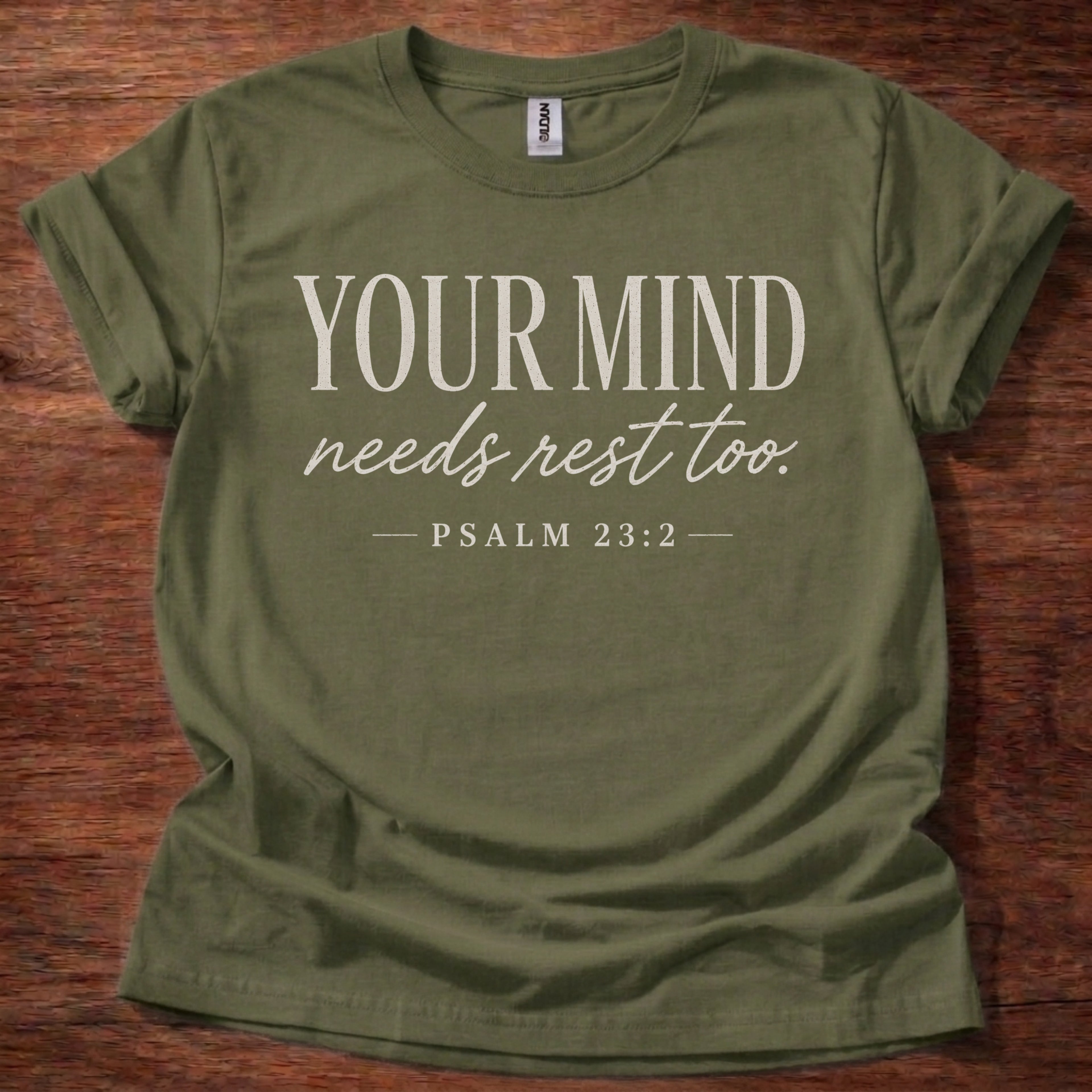 Green t-shirt with 'Your Mind Needs Rest Too' text on a wooden surface