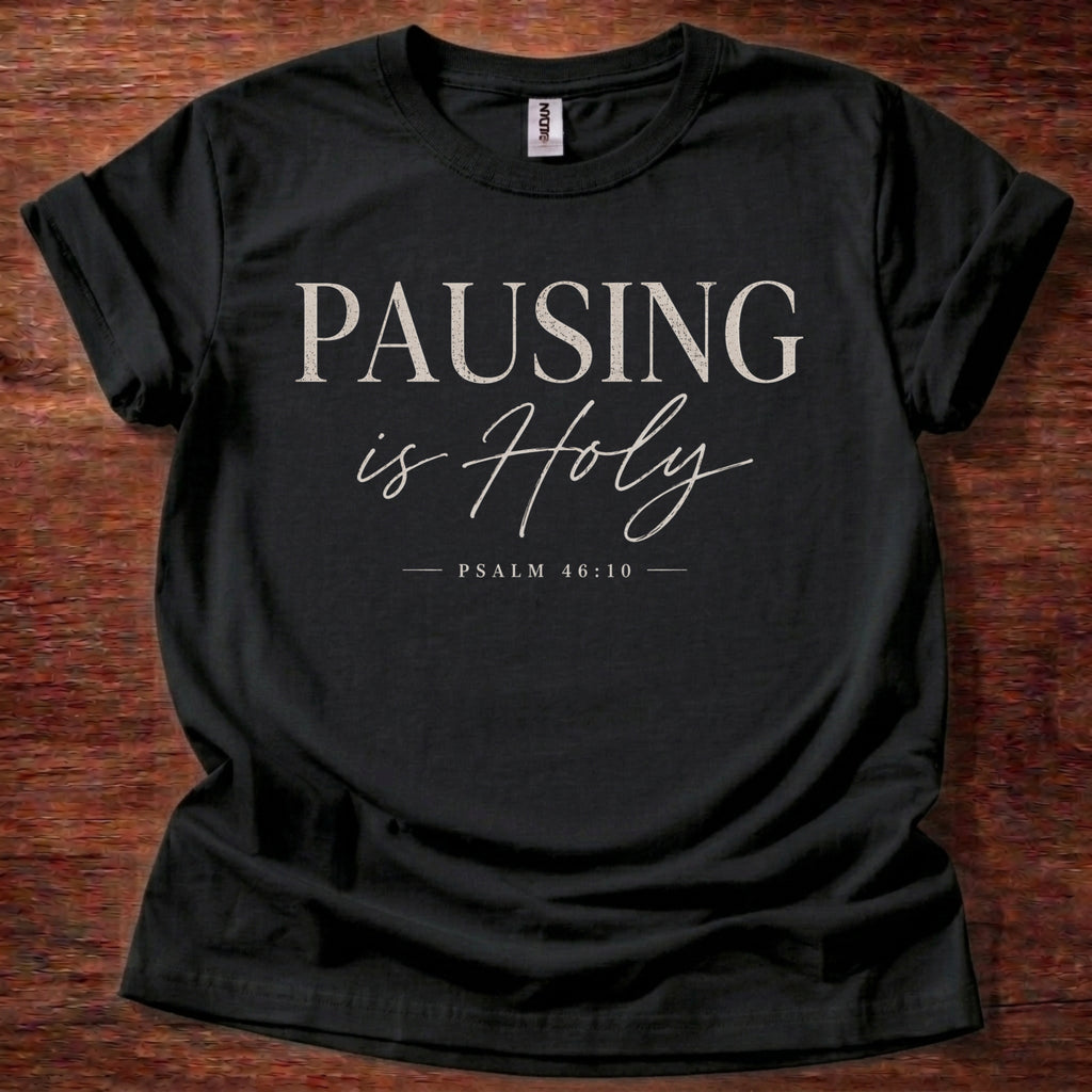 Black t-shirt with 'PAUSING is Holy' text on a wooden surface