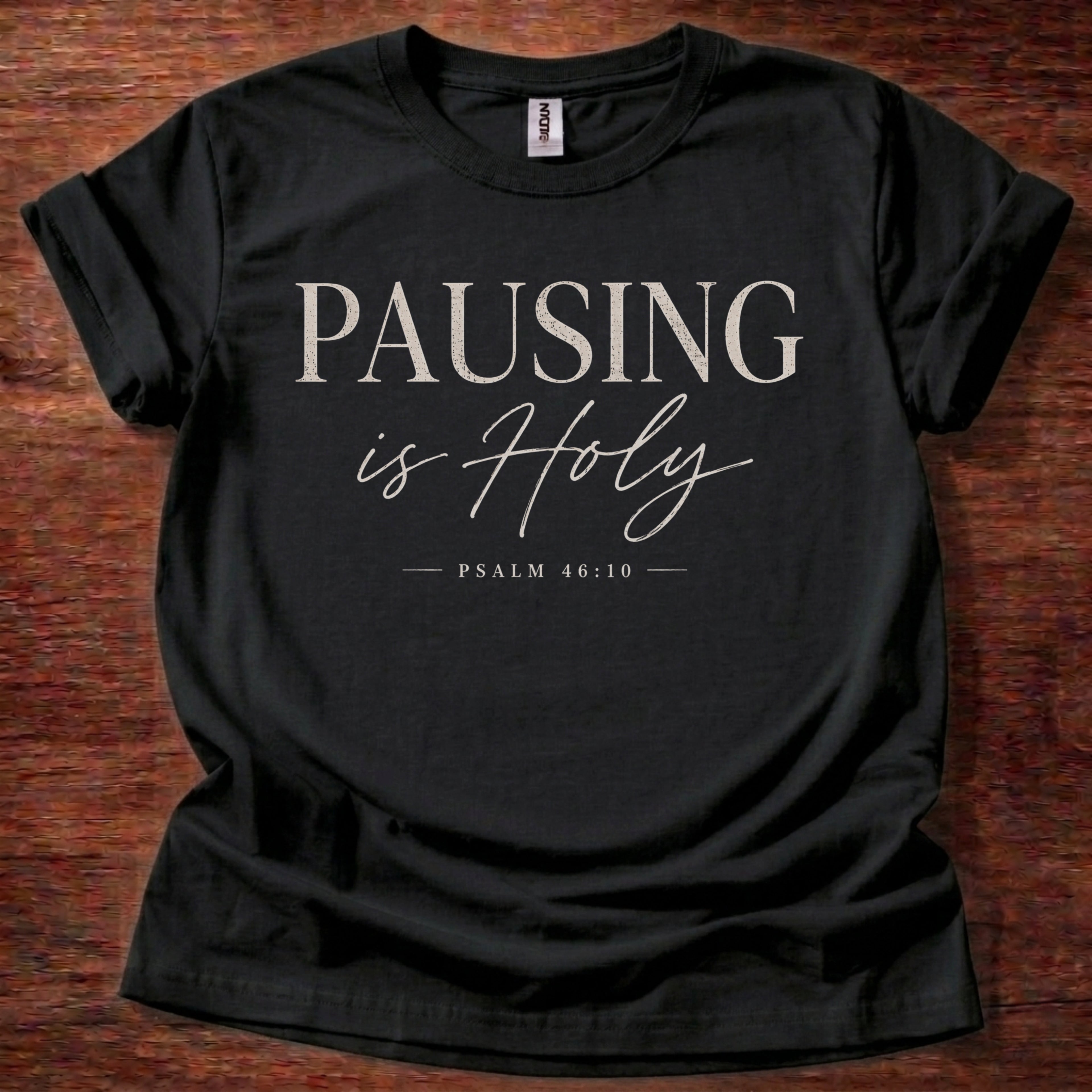 Black t-shirt with 'PAUSING is Holy' text on a wooden surface