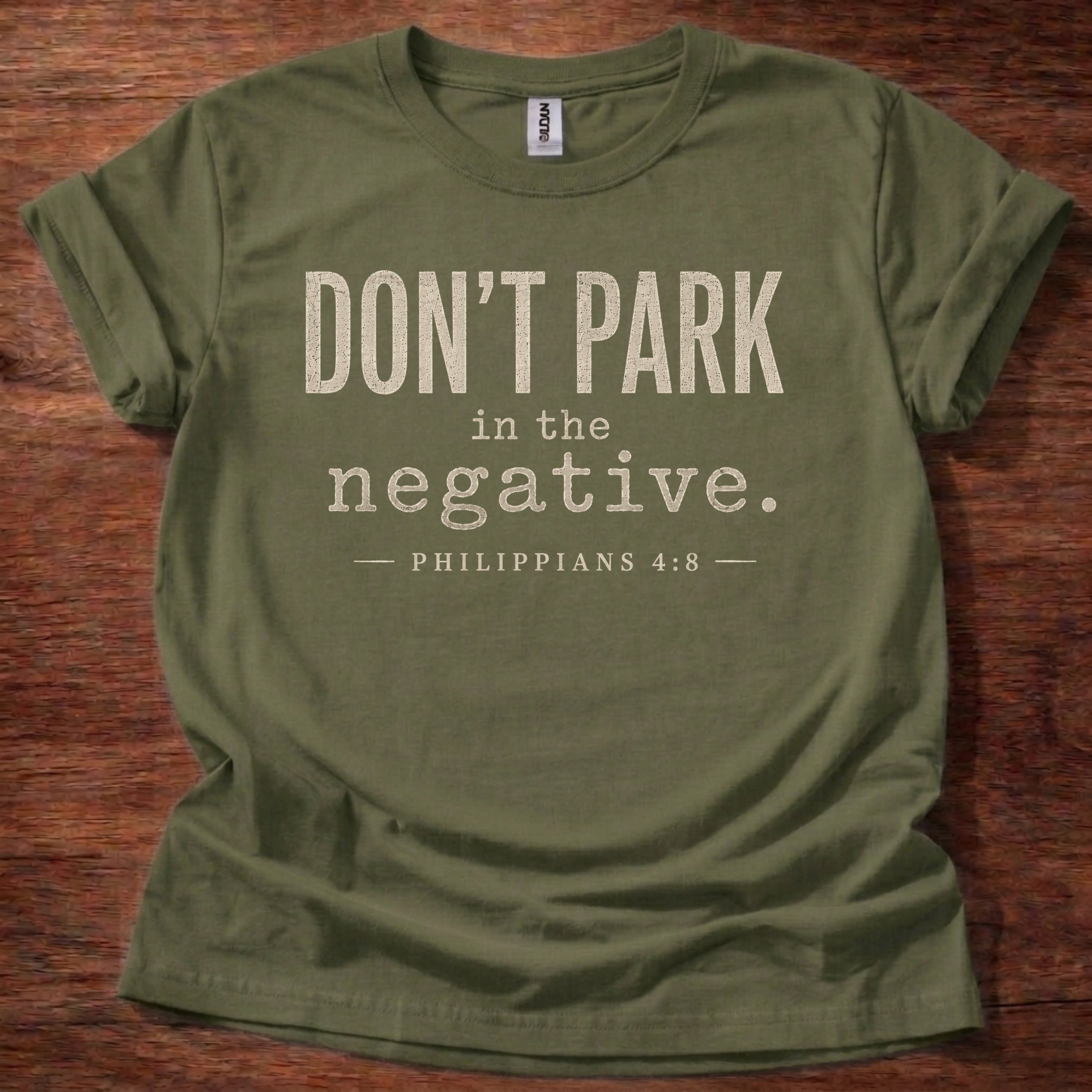 Green t-shirt with text 'DON'T PARK in the negative. PHILIPPIANS 4:8' on a wooden surface