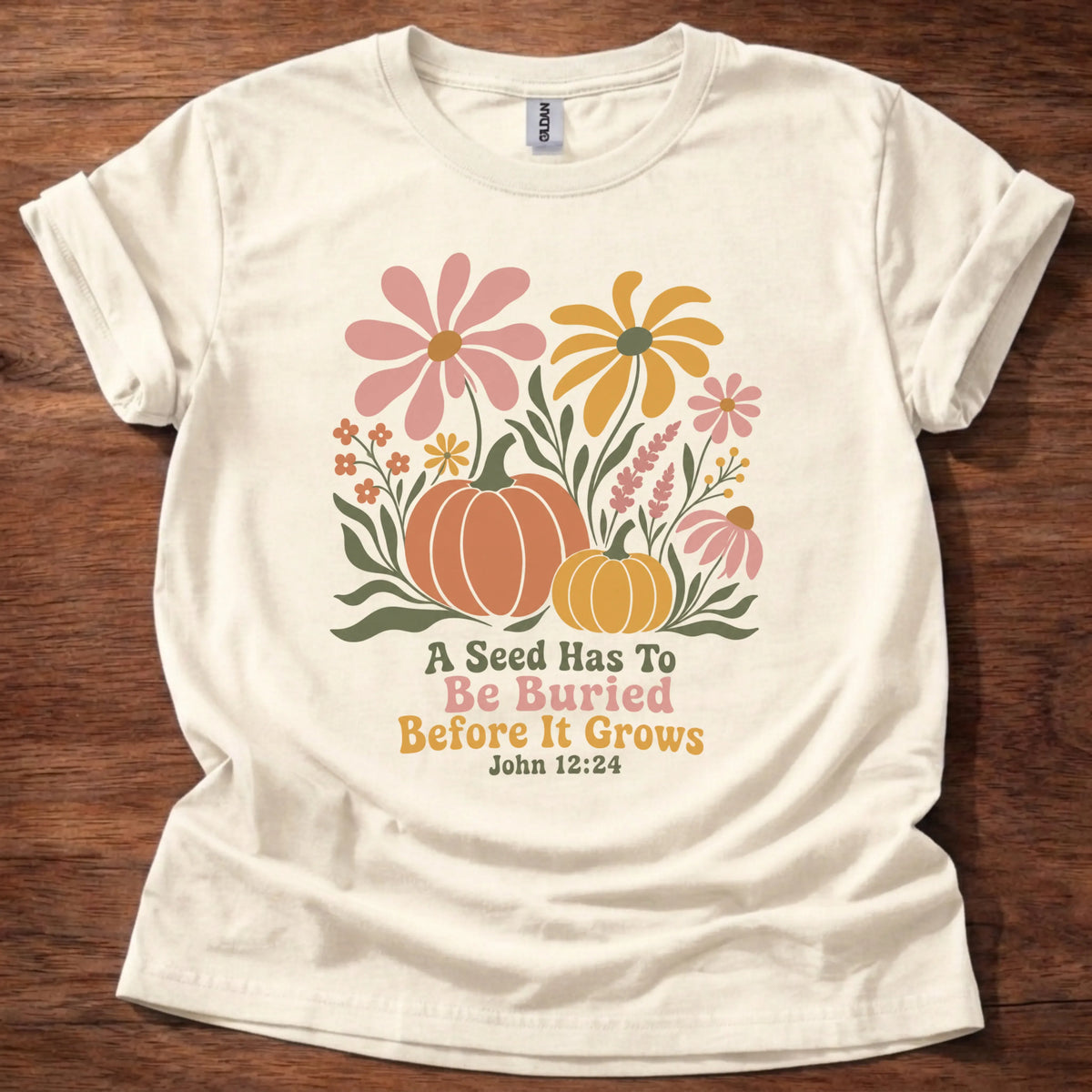 Colorful wildflower and pumpkin illustration t-shirt with retro lettering reading 'A Seed Has To Be Buried Before It Grows' — John 12:24