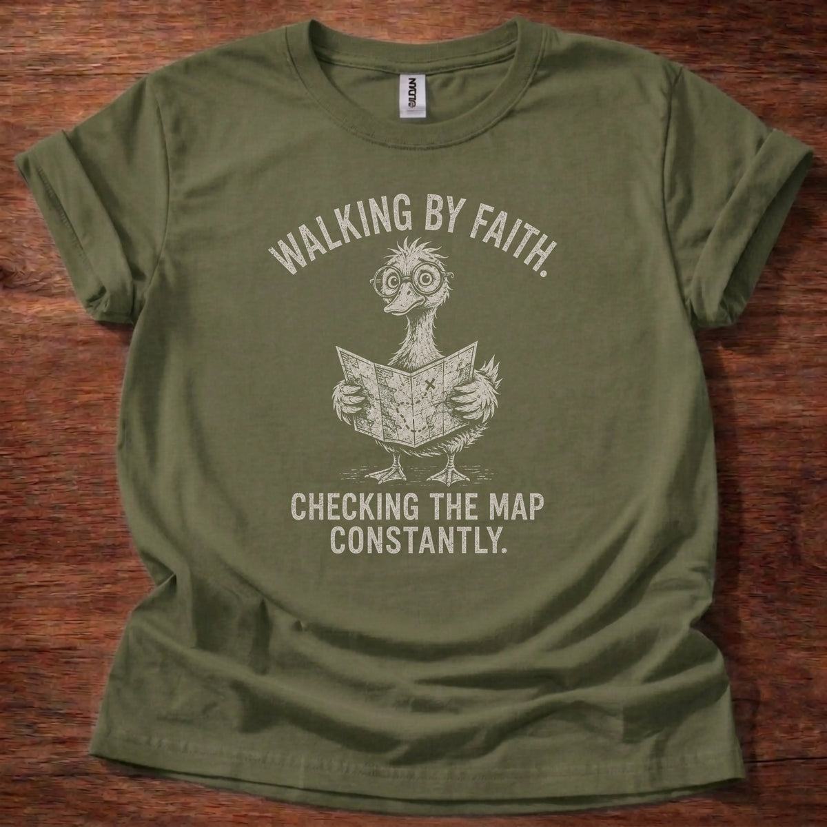 White fine-line illustration of a duck reading a map wearing glasses with the text 'Walking By Faith. Checking The Map Constantly.'