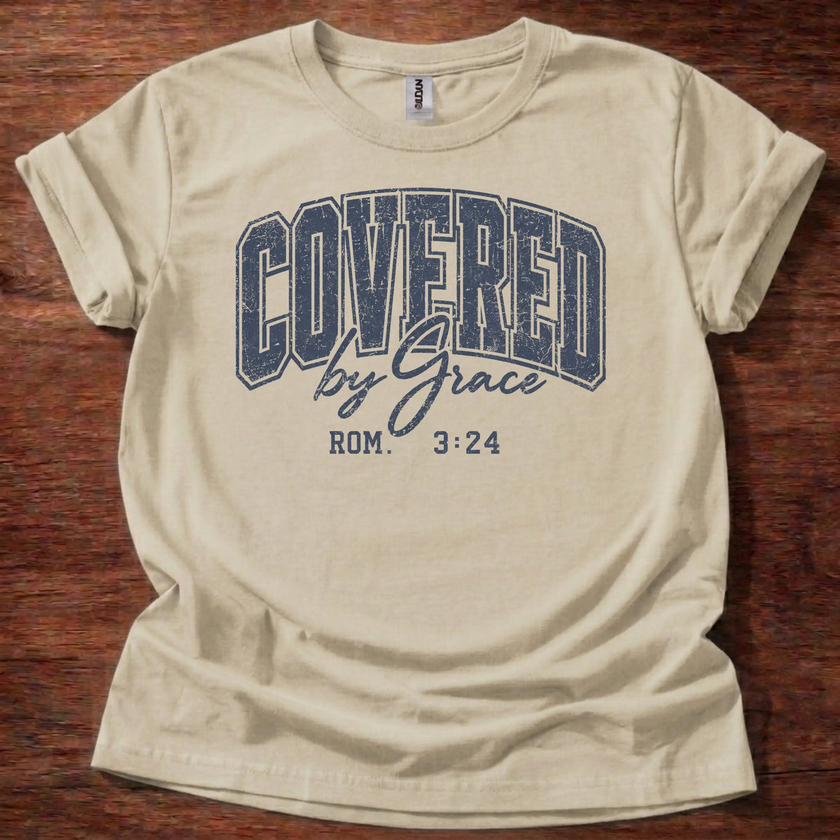 Navy distressed varsity-style t-shirt reading 'Covered by Grace' with cursive script and Romans 3:24 citation