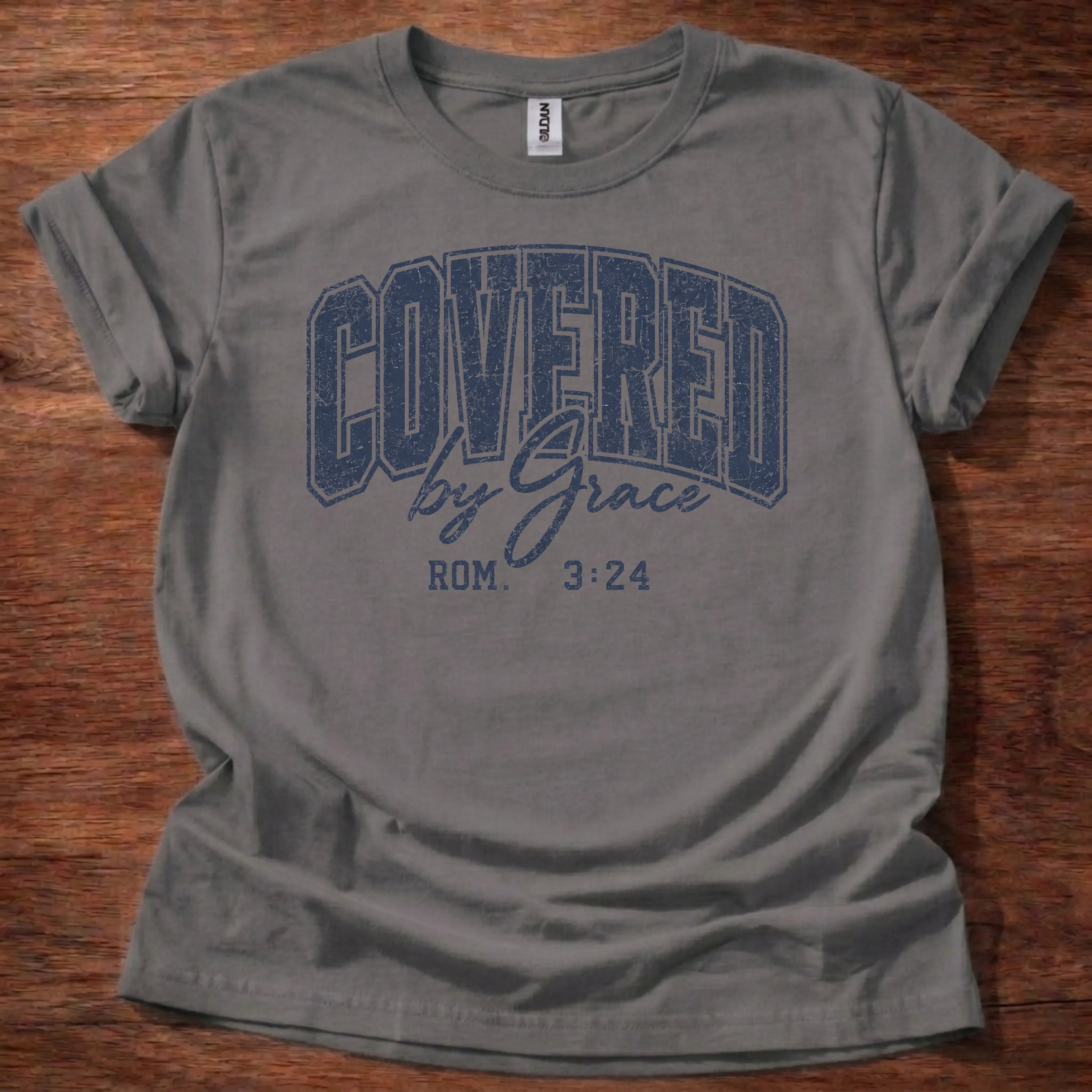 Navy distressed varsity-style t-shirt reading 'Covered by Grace' with cursive script and Romans 3:24 citation