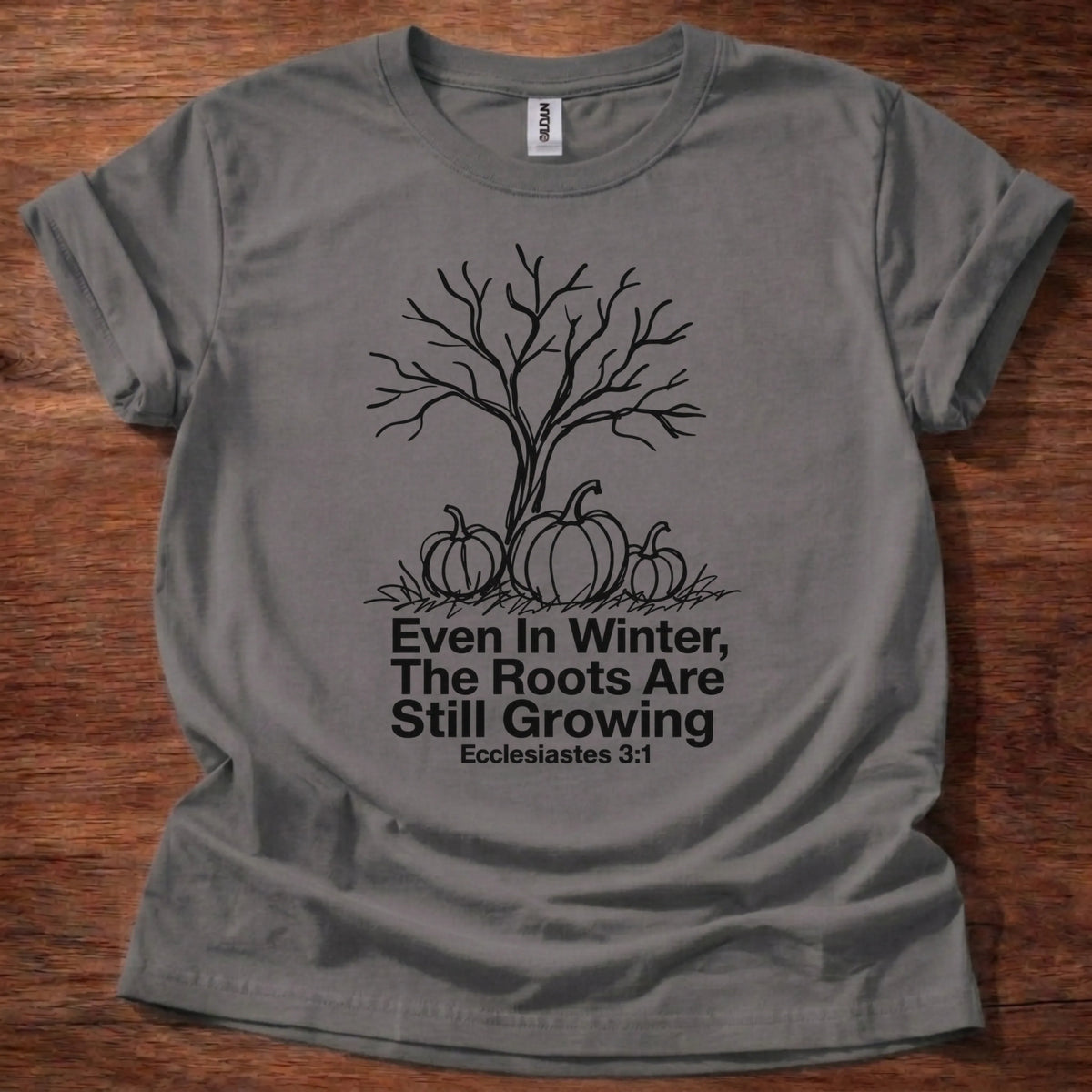 Bold black and white illustration t-shirt of a bare winter tree over a pumpkin patch with the text 'Even In Winter, The Roots Are Still Growing' — Ecclesiastes 3:1