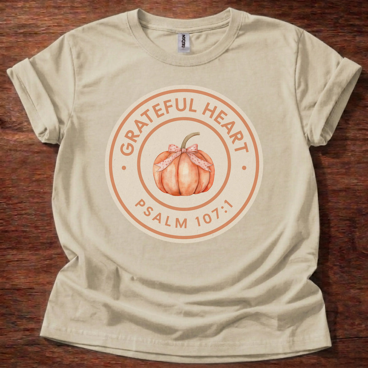 Circular badge t-shirt with a watercolor pumpkin illustration and the text 'Grateful Heart' and 'Psalm 107:1' arched around the ring