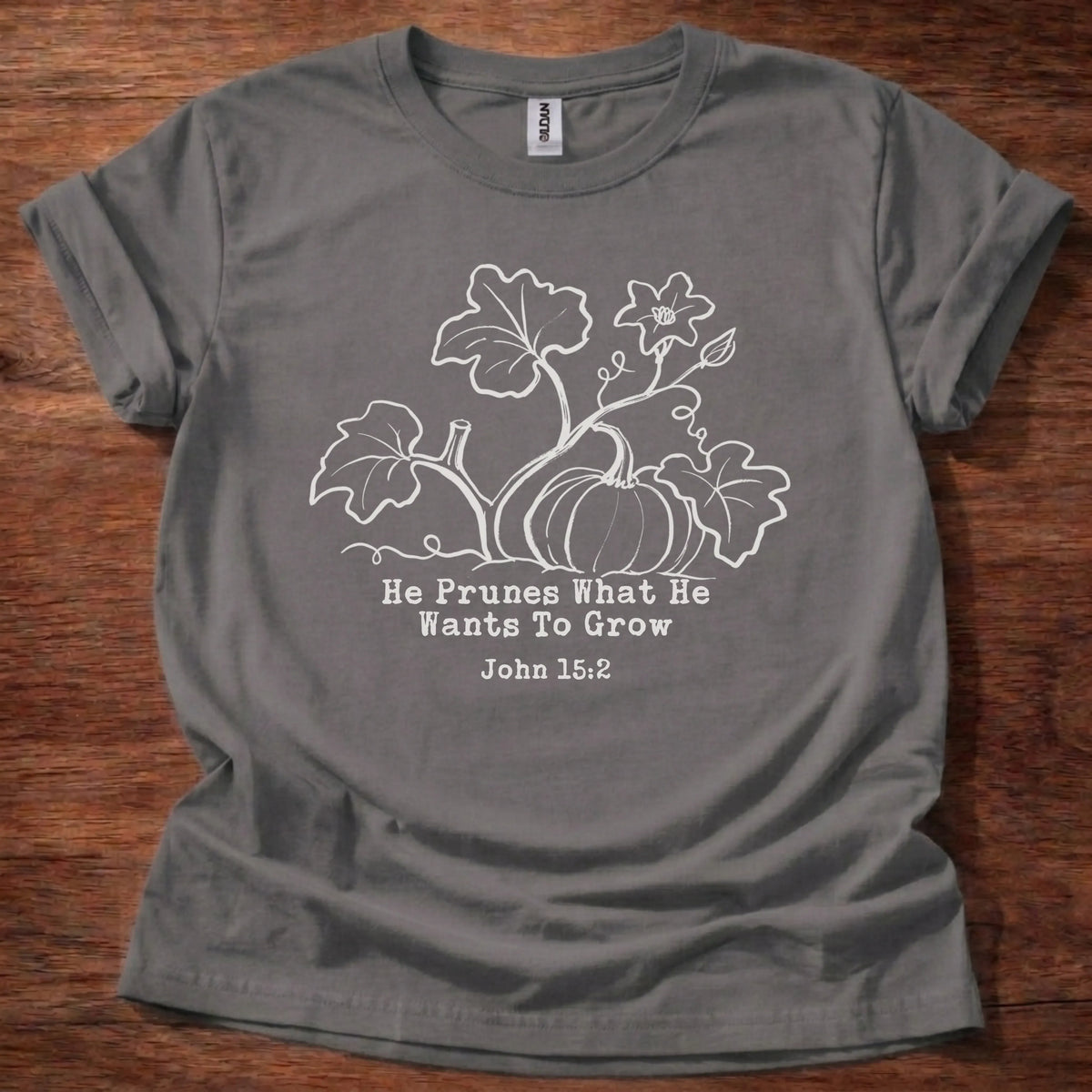 Cream tonal pumpkin vine illustration t-shirt with the text 'He Prunes What He Wants To Grow' and John 15:2