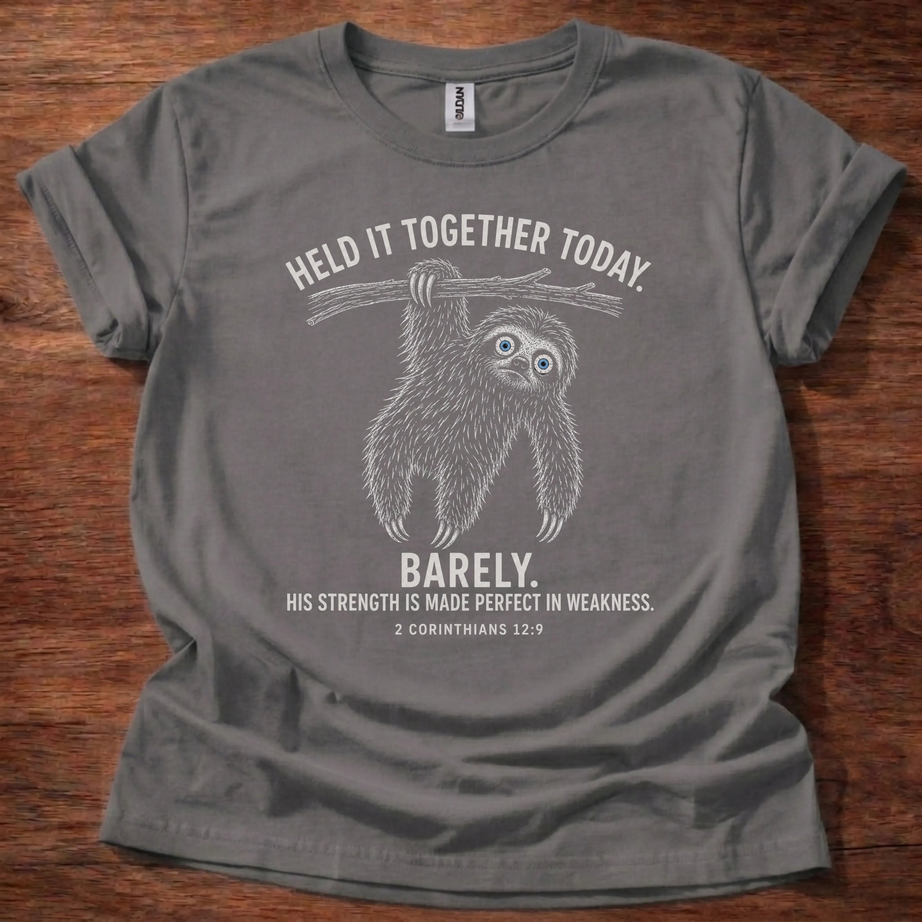 White fine-line sloth illustration hanging from a branch t-shirt with the text 'Held It Together Today. Barely.' and 2 Corinthians 12:9