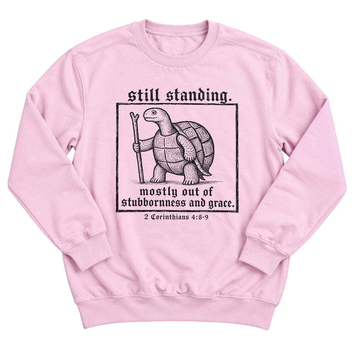 Light pink crewneck sweatshirt with a woodcut-style tortoise with a walking stick inside a framed box and the words Still Standing. Mostly Out Of Stubbornness And Grace. 2 Corinthians 4:8-9