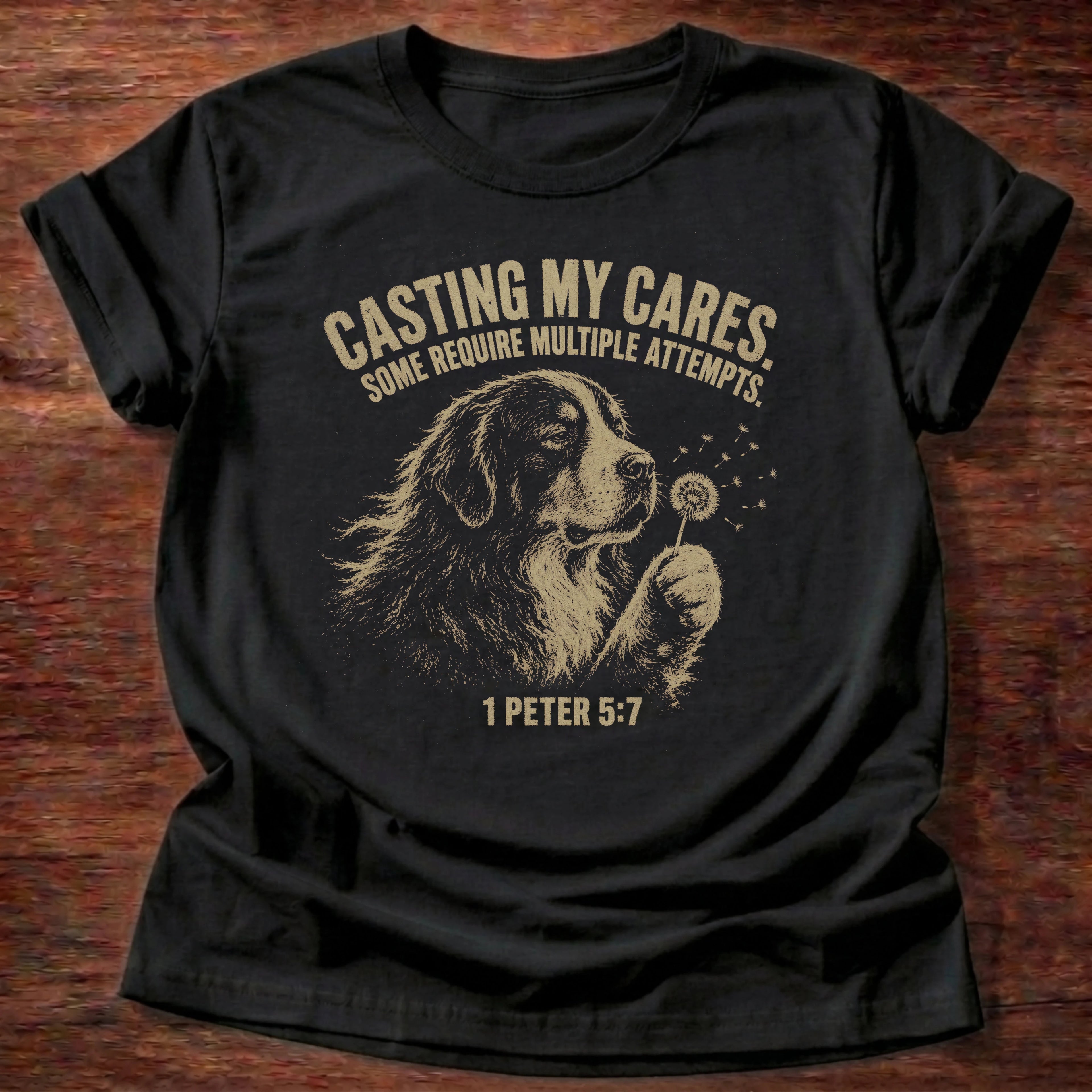 Black t-shirt with a dog illustration holding a dandelion reading 'Casting my cares, some require multiple attempts' 1 Peter 5:7 shirt