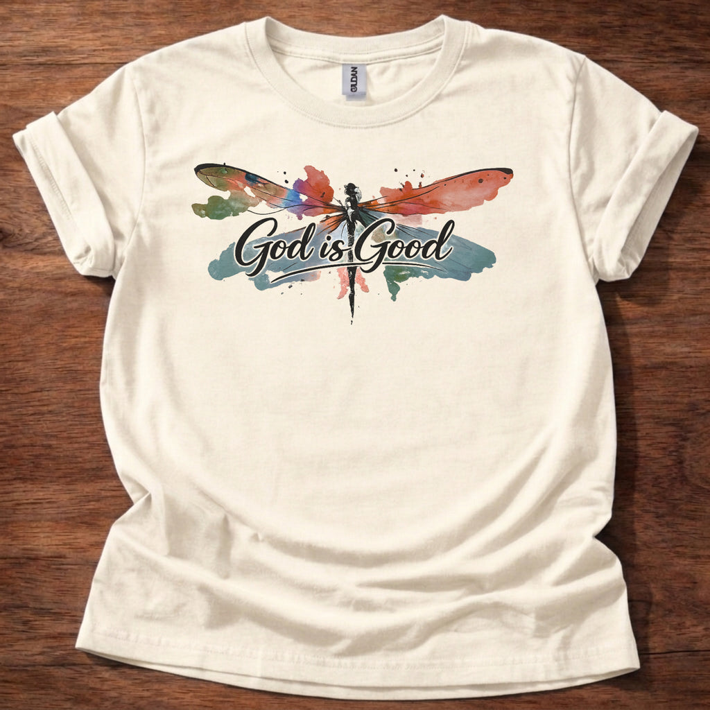Natural  t-shirt featuring a colorful watercolor dragonfly design with the words “God is Good” printed across the front