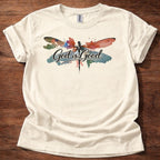 Natural  t-shirt featuring a colorful watercolor dragonfly design with the words “God is Good” printed across the front