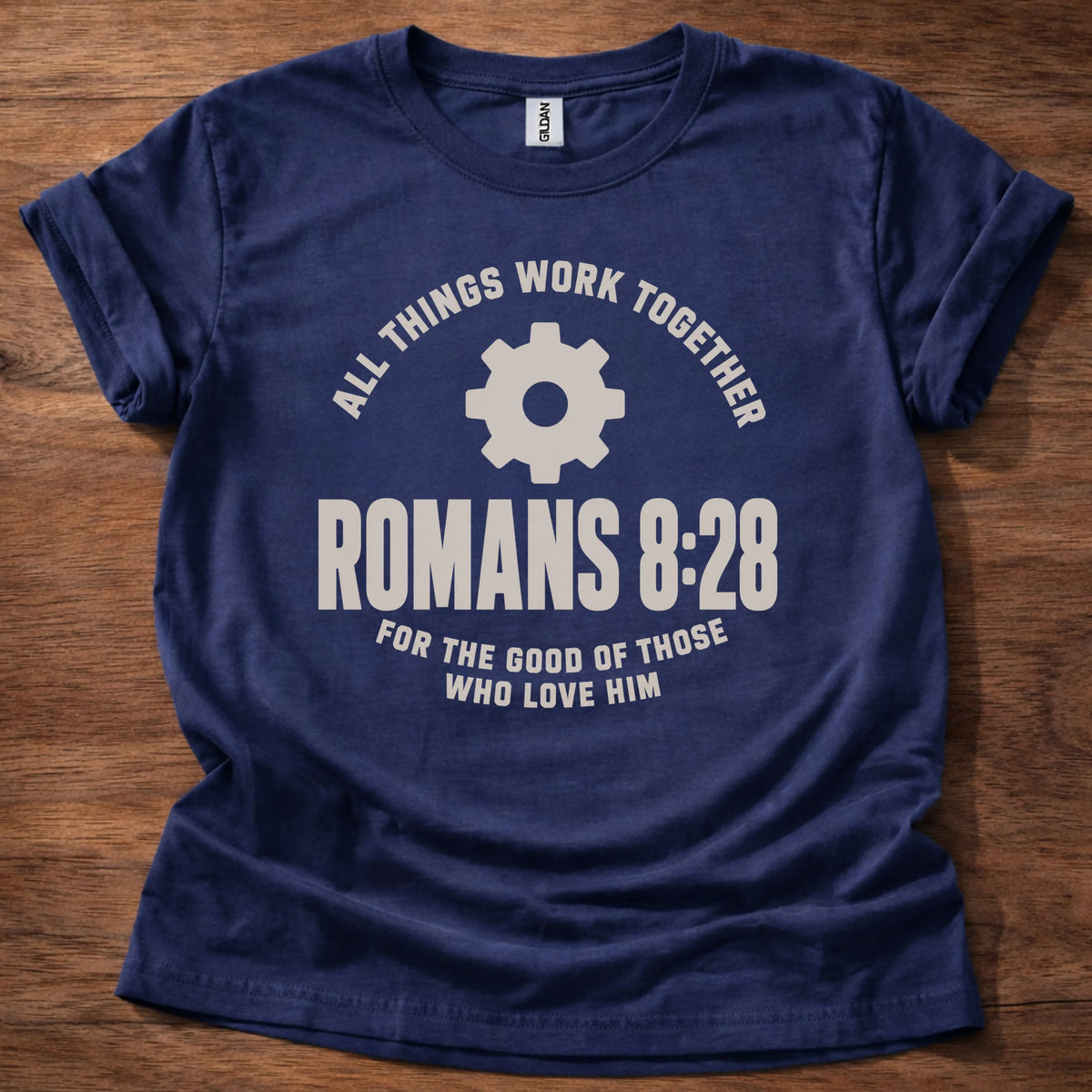 Cream gear icon t-shirt with the text 'All Things Work Together' arched above and 'Romans 8:28' below