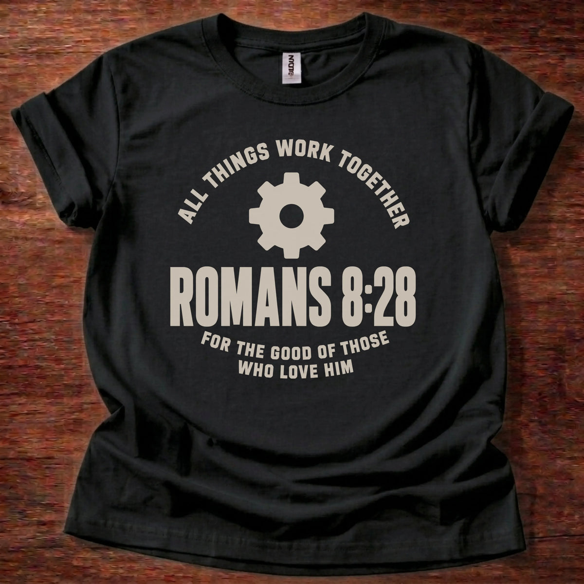 Cream gear icon t-shirt with the text 'All Things Work Together' arched above and 'Romans 8:28' below