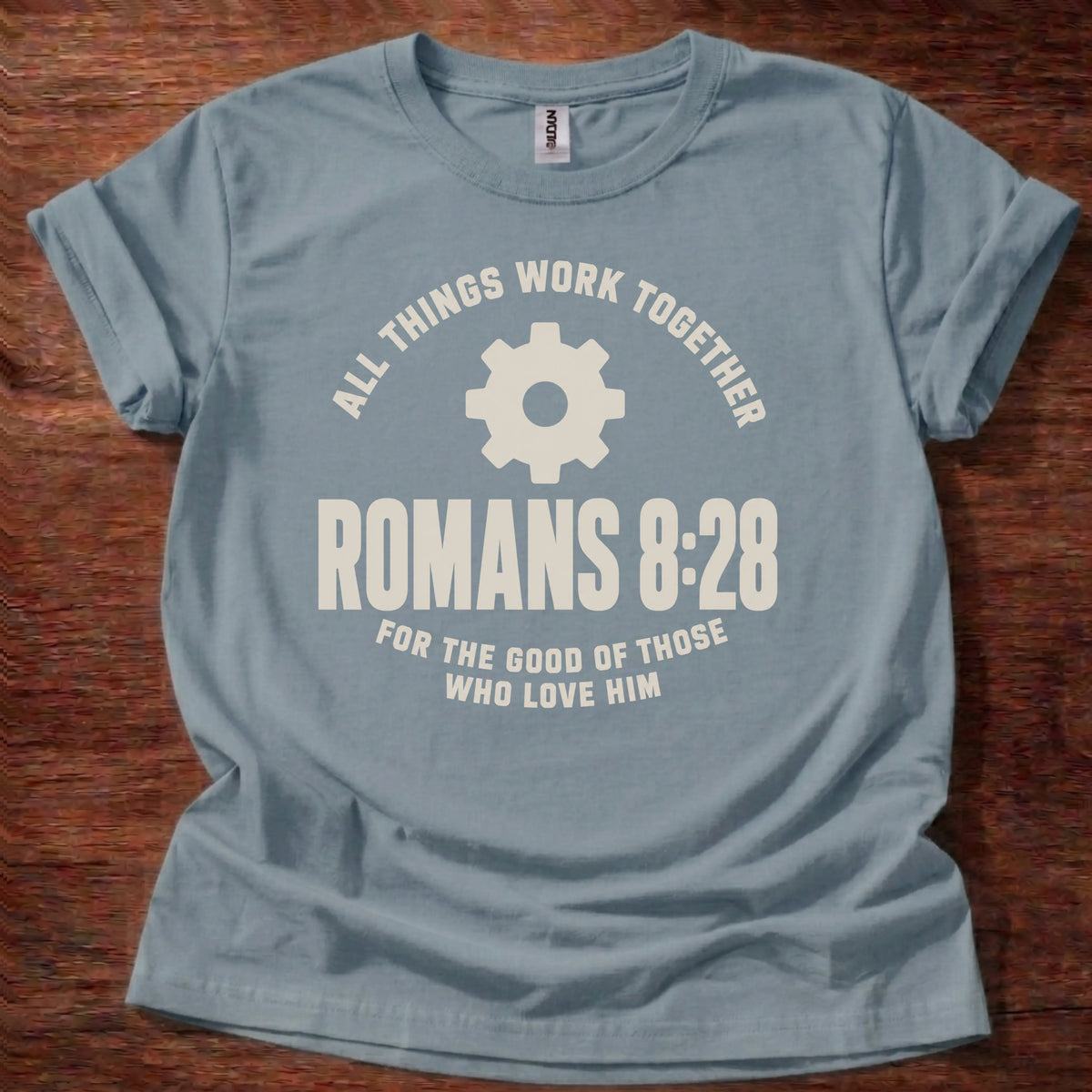 Cream gear icon t-shirt with the text 'All Things Work Together' arched above and 'Romans 8:28' below