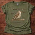 An olive green short-sleeve t-shirt with a brown graphic print of a sparrow perched on a branch, labeled 'SPARROW STUDY' with scripture references and callout lines, laid flat on a dark wood background.