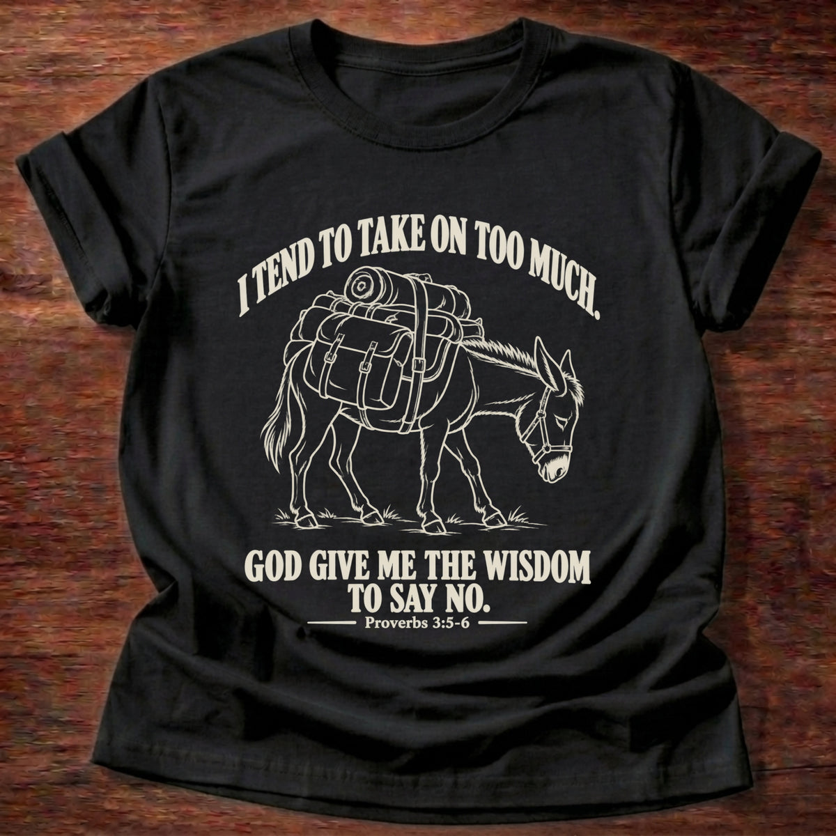 Black t-shirt printed with a pack donkey weighed down with overstuffed bags and bundles graphic and “I tend to take on too much. God give me the wisdom to say no.” Proverbs 3:5-6 faith based gift