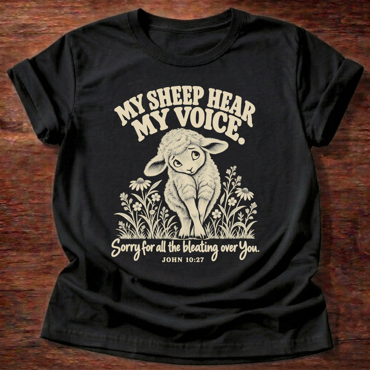 Jesus' Voice T-Shirt in Black featuring a lamb standing among wildflowers and John 10:27 good shepherd humor design