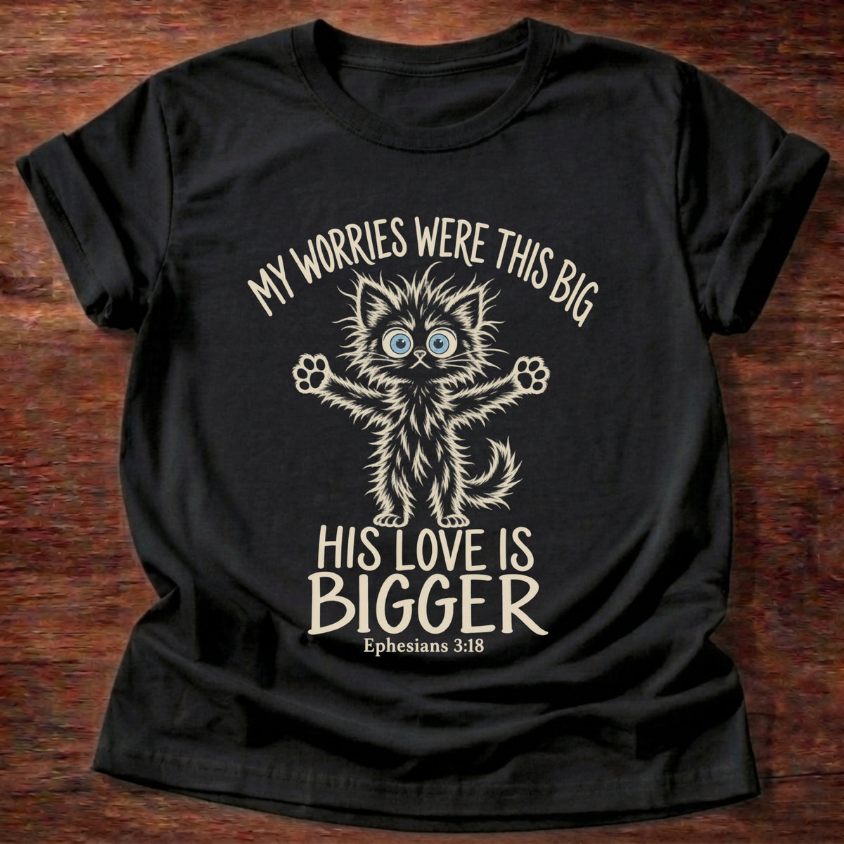 Black t-shirt printed with a wide-eyed fluffy kitten stretching its arms wide graphic and “My worries were this big. His love is bigger.” Ephesians 3:18 Christian shirt