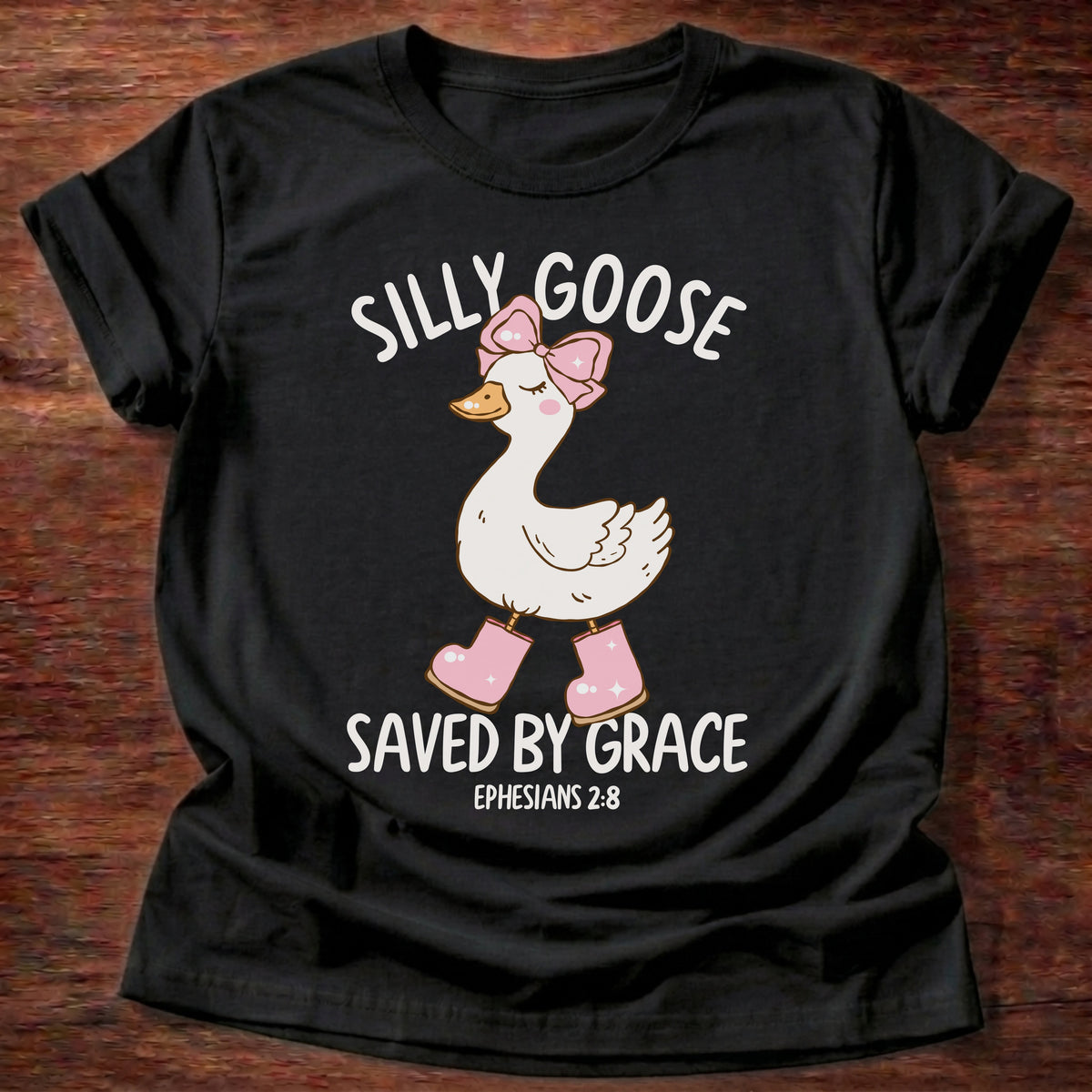 Black t-shirt printed with a goose wearing a pink bow and pink boots and “Silly Goose. Saved by Grace.” Ephesians 2:8 Christian shirt