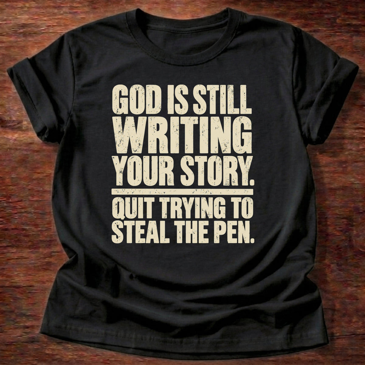 Black t-shirt printed with bold stacked typography graphic and “God is still writing your story. Quit trying to steal the pen.” Philippians 1:6 Christian shirt
