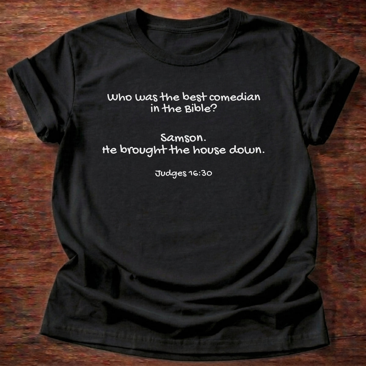 Black t-shirt printed with a simple hand-lettered Bible joke graphic and “Who was the best comedian in the Bible? Samson. He brought the house down.” Judges 16:30 Christian shirt