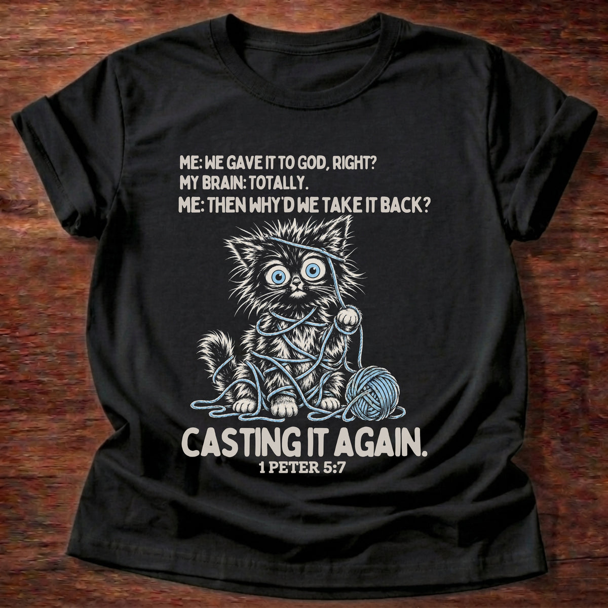 Black t-shirt printed with a wide-eyed kitten tangled in yarn graphic and “Me: We gave it to God, right? My brain: Totally. Me: Then why'd we take it back? Casting it again.” 1 Peter 5:7 Christian shirt
