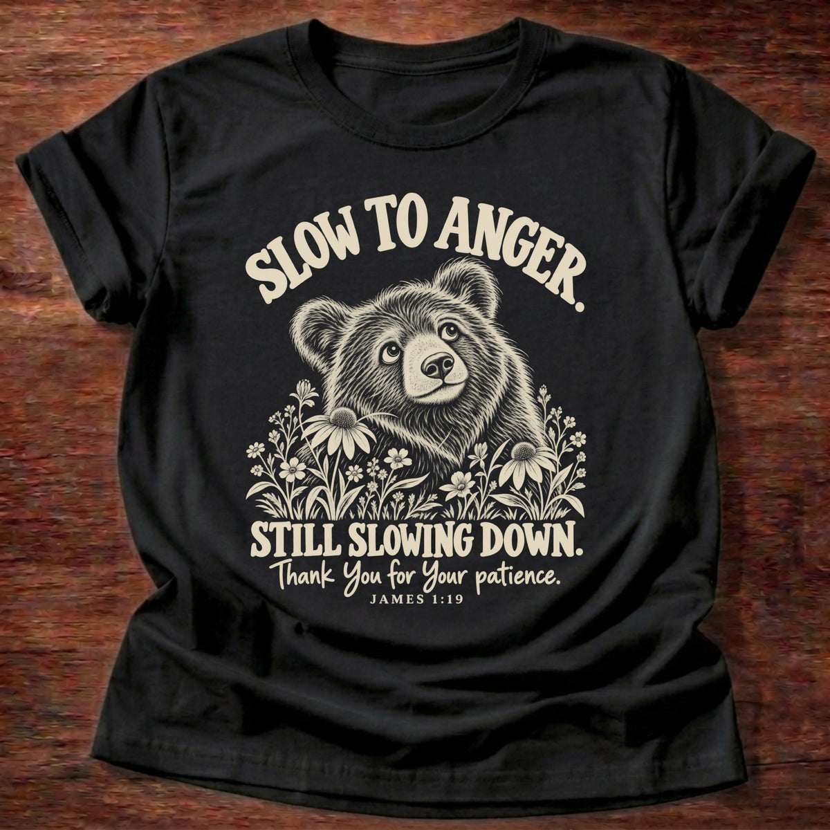Still Slowing Down T-Shirt in Black featuring a bear cub resting among wildflowers and James 1:19 patience humor design