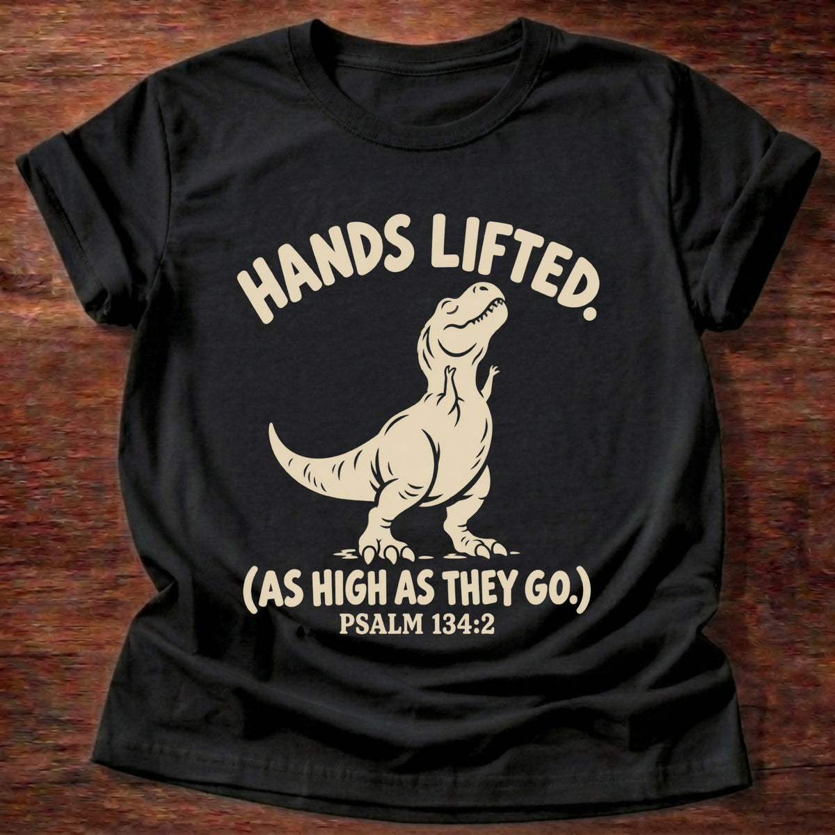 Black t-shirt printed with a T-rex with tiny raised arms graphic and “Hands lifted. (As high as they go.)” Psalm 134:2 Christian shirt