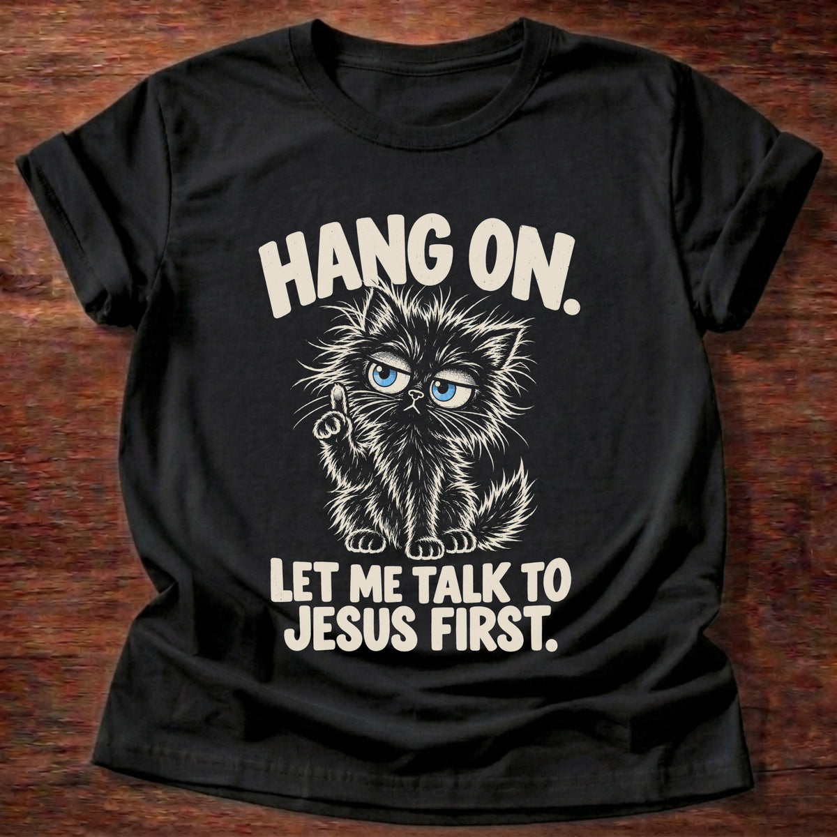 Black t-shirt printed with a frazzled fluffy kitten holding up one finger graphic and “Hang on. Let me talk to Jesus first.” faith based gift