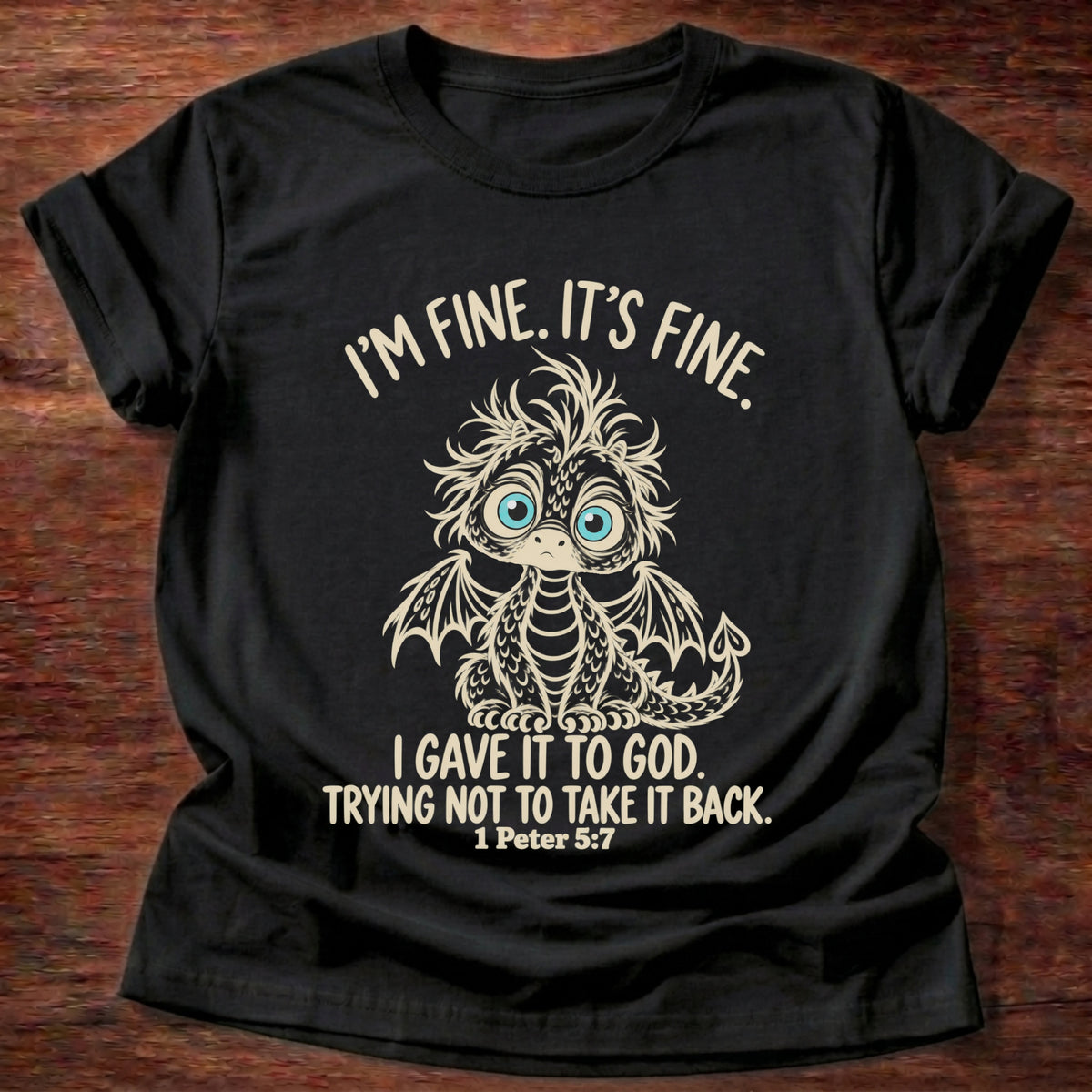Black t-shirt printed with a wide-eyed, frazzled baby dragon graphic and “I'm fine. It's fine. I gave it to God. Trying not to take it back.” 1 Peter 5:7 Christian shirt
