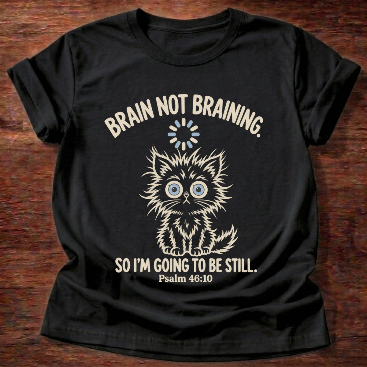 Black t-shirt printed with a wide-eyed fluffy kitten graphic and “Brain not braining. So I'm going to be still.” Psalm 46:10 Christian shirt
